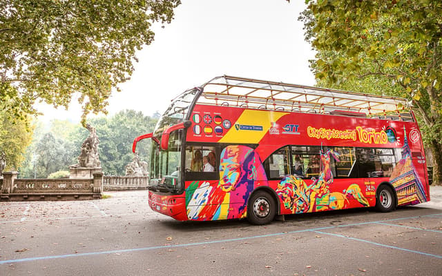 Colourful open-top City Sightseeing double-decker bus on a tree-lined avenue in Turin