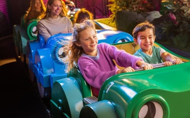 Children riding a green caterpillar coaster on a colourful indoor family ride in Antwerp