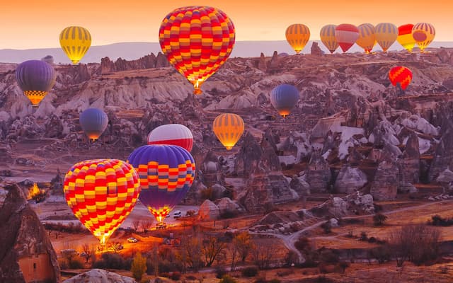 Colourful hot air balloons rising over Cappadocia rock valleys at sunrise