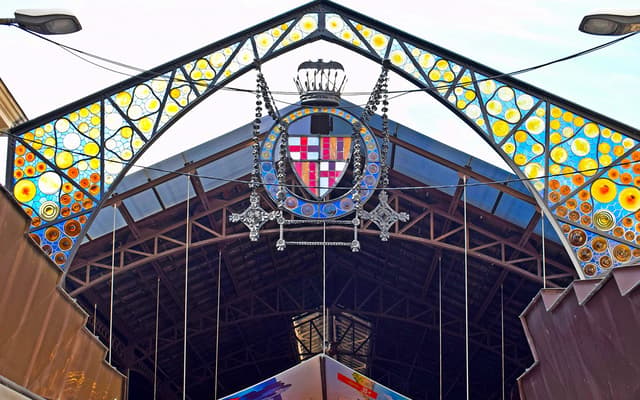 Stained-glass and ironwork entrance arch of a Barcelona market with the city crest