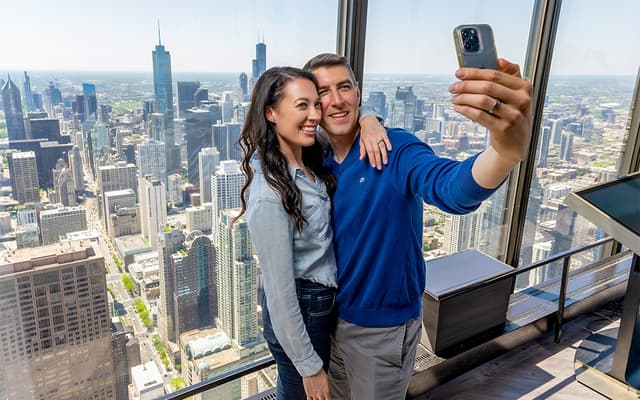 Couple taking a selfie at a high-rise observation deck with the Chicago skyline behind the glass