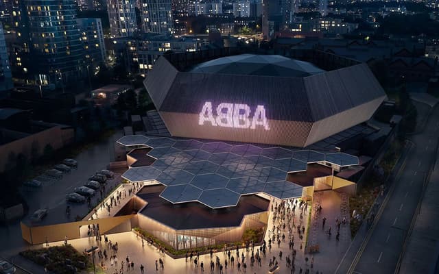 ABBA Arena lit up at night in London with the ABBA logo glowing on the hexagonal dome