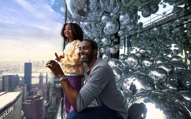 Couple at a mirrored New York observation deck with the Manhattan skyline behind them
