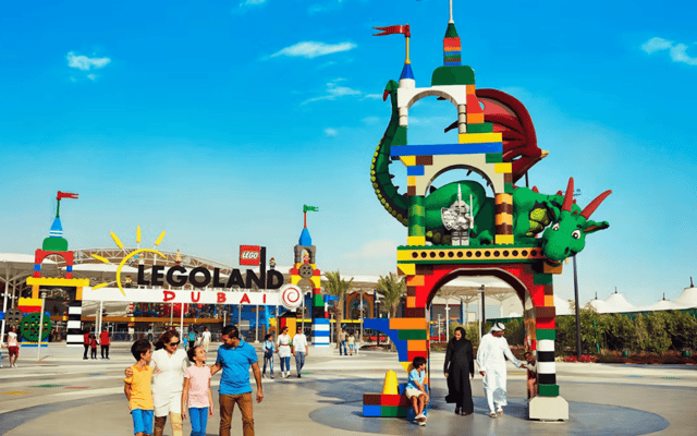 Families at the LEGOLAND Dubai entrance beside a giant LEGO dragon sculpture under blue sky