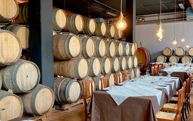 Stacked wine barrels beside a long set dining table in a Florence wine cellar restaurant