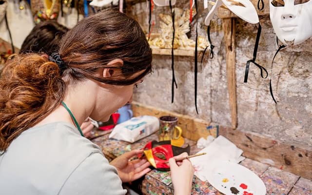 Artisan hand-painting a red and gold Venetian carnival mask in a Venice workshop