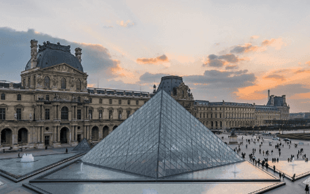 The glass Louvre Pyramid and palace courtyard at sunset in Paris