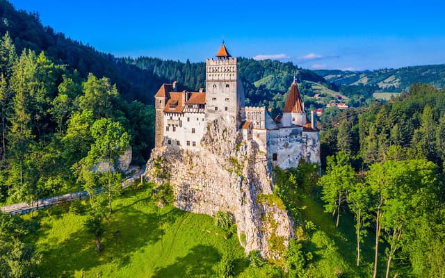 Bran Castle perched on a forested clifftop in Transylvania, Romania under blue sky