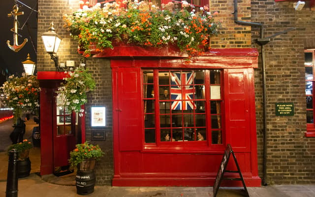 Traditional red-fronted London pub at dusk with hanging flower baskets and a Union Jack in the window
