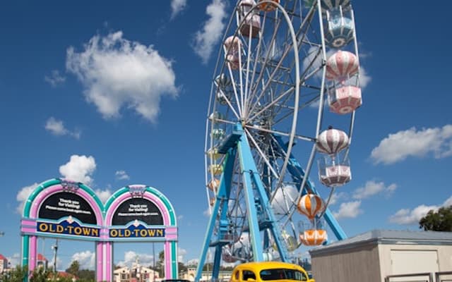 Old Town Kissimmee entrance arch and Ferris wheel with a yellow classic car under a blue sky