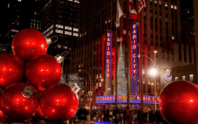 Radio City Music Hall lit up at night with giant red Christmas baubles in New York