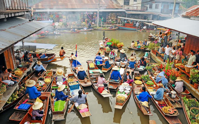 Wooden boats laden with produce and vendors in conical hats at a Bangkok floating market