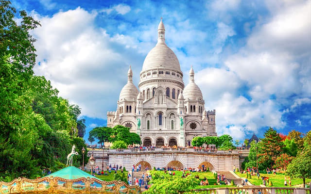 White-domed Sacre-Coeur Basilica in Montmartre, Paris, with a carousel and green gardens in front