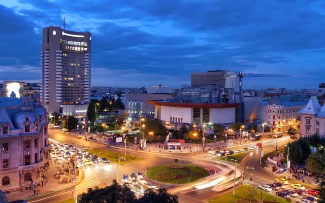 Bucharest city centre lit up at dusk with a busy roundabout and modern high-rise towers