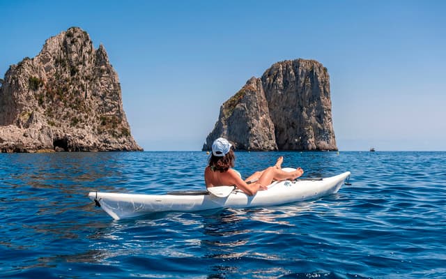 Woman relaxing in a white kayak on turquoise water by the Faraglioni rock stacks off Capri