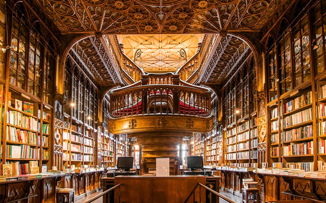 Carved wood staircase and stained-glass ceiling inside Livraria Lello bookshop in Porto
