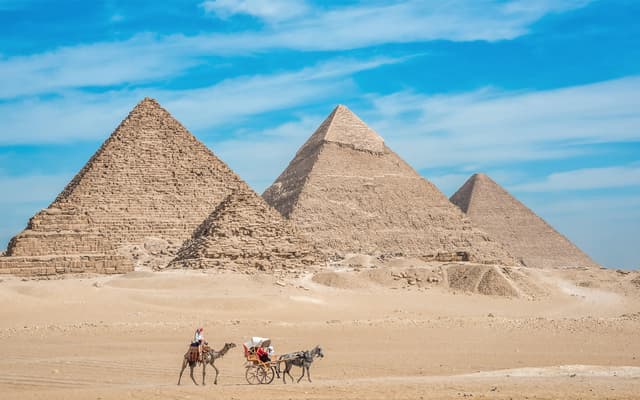 Pyramids of Giza in the Cairo desert with a camel rider and horse carriage in front