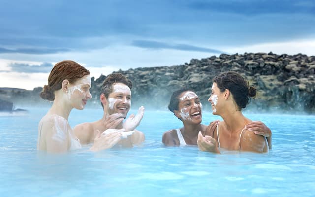 Four friends relaxing with silica face masks in a steaming geothermal spa among Iceland's lava rocks