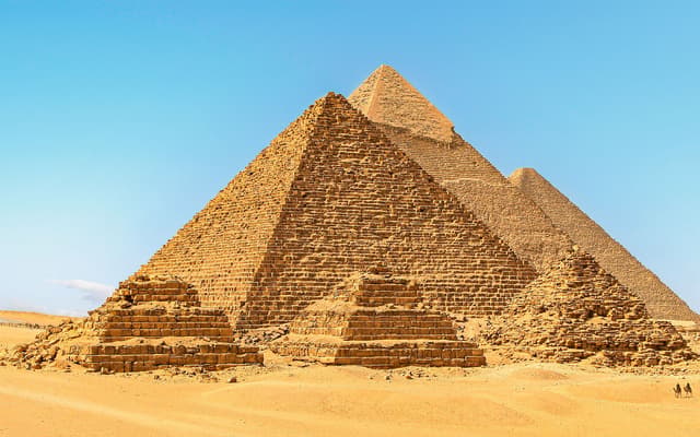 The three Pyramids of Giza under a blue sky with golden desert sand near Cairo