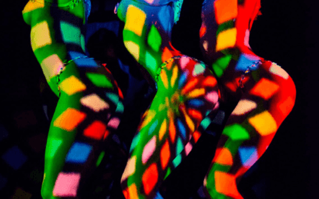 Cabaret dancers in glittering caps lit by colourful kaleidoscope projections at a Paris show