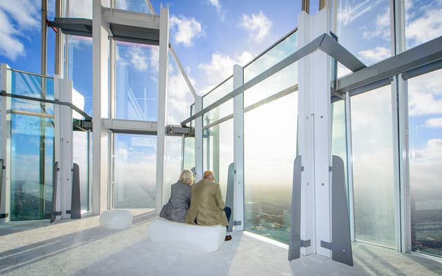 Couple seated at the glass viewing gallery looking out over London from a tall tower
