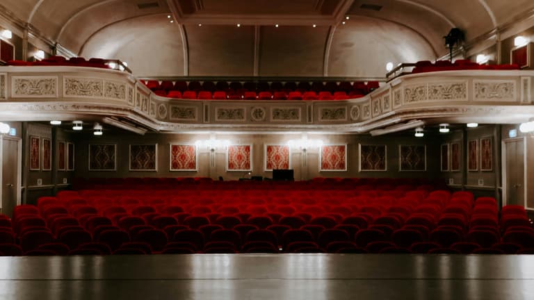 The interior of a grand West End theatre with red seats across the stalls and circle levels