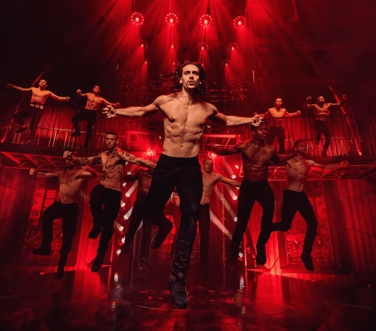 Shirtless male dancers leaping under red stage lights at a London immersive dance show