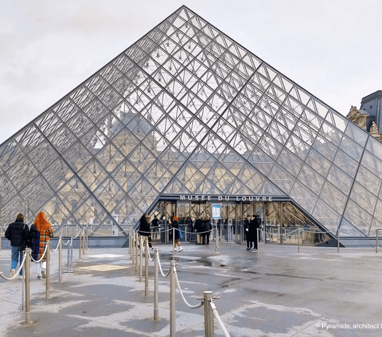 Visitors gathered at the Louvre glass pyramid courtyard in daytime Paris