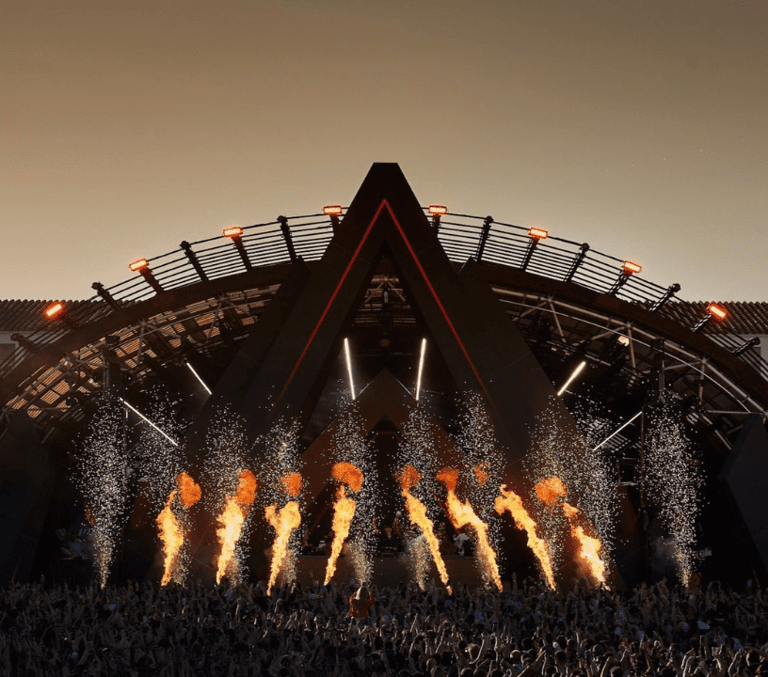 Ushuaia Ibiza main stage in red light above a dense daytime pool party crowd