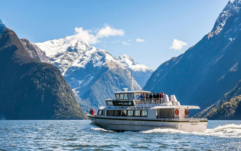 Mitre Peak rising sheer above the dark water of Milford Sound with a cruise boat below
