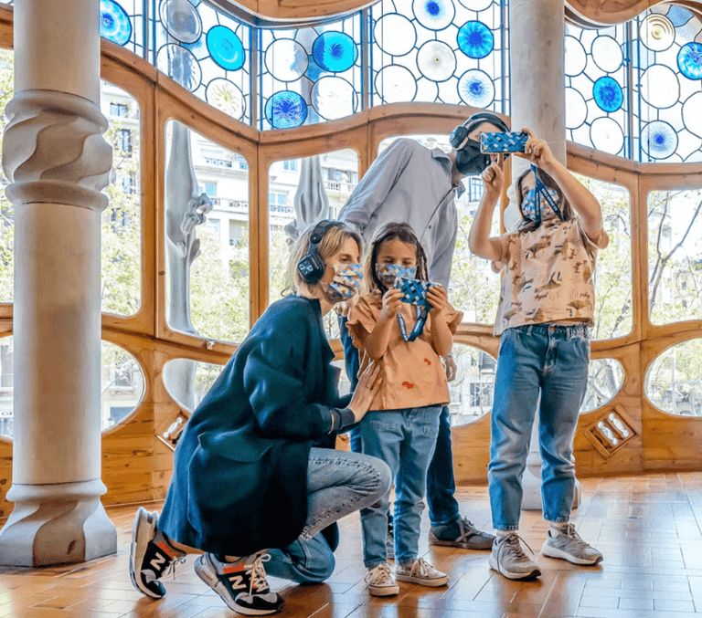 Family using audio headsets in the stained-glass interior of Casa Batllo in Barcelona