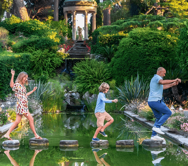Family hopping across stepping stones over a garden pond on the French Riviera
