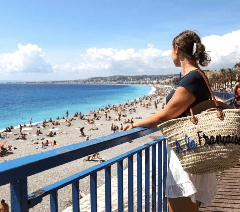 Woman with straw bag looking out over the beach and turquoise bay in Nice on the French Riviera