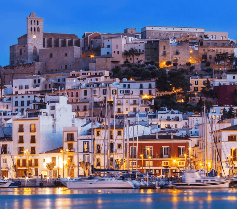 Hilltop old town and harbour boats lit up at dusk on the French Riviera coast
