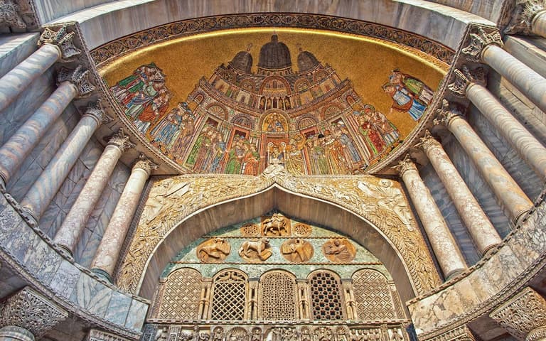 The golden mosaics and ornate carved stone above the main doorway of St Mark's Basilica in Venice