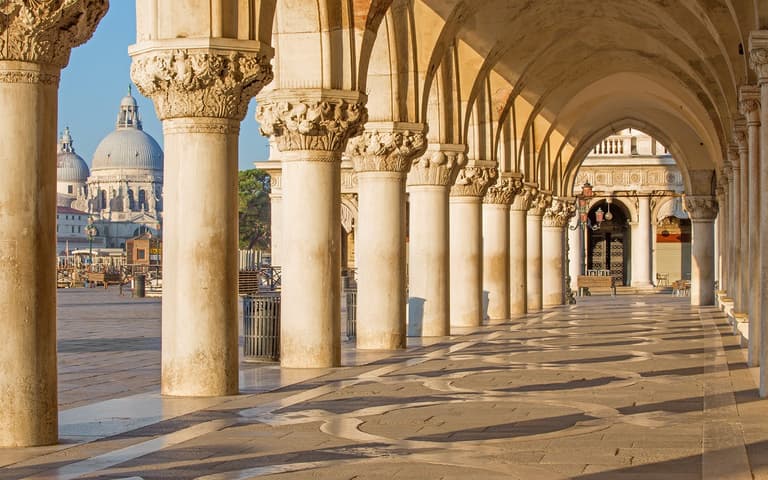 The marble colonnade of the Doge's Palace on St Mark's Square, looking out towards the domed church of Santa Maria della Salute