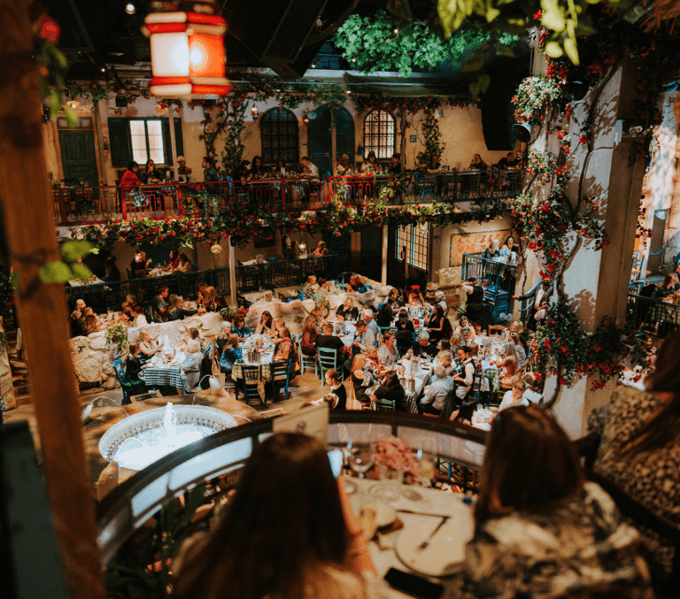 The Mamma Mia! The Party taverna courtyard seen from above at night, with tables across the ground floor and terraces lit by festoon lights