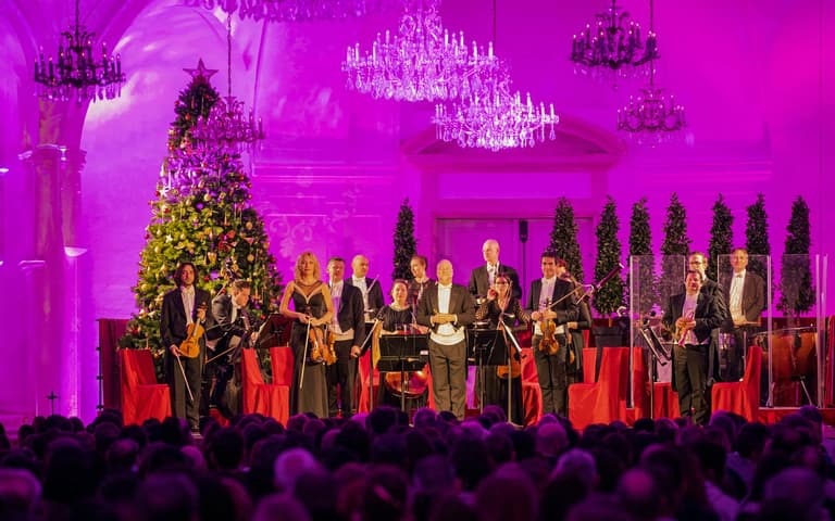 An orchestra and singers performing beside a Christmas tree at a Schönbrunn Palace Christmas concert