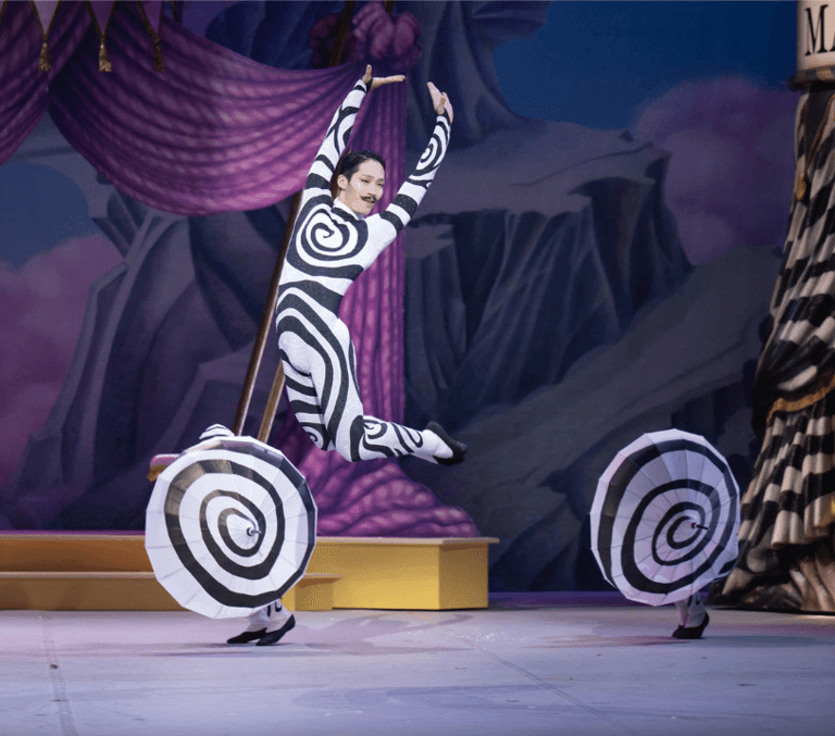 ENB Nutcracker, a dancer in a black and white swiled body suit leaps centre stage.