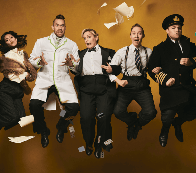 Broadway cast in suits and uniforms leaping mid-air as papers fly around them
