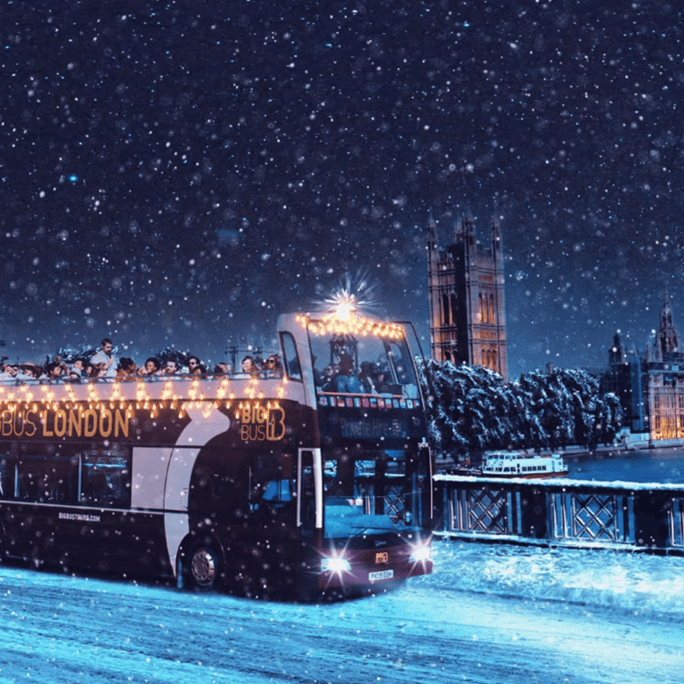 Big Bus London open-top tour bus in falling snow by the Houses of Parliament at night