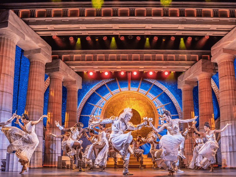 The company of Disney's Hercules dancing on stage at the Theatre Royal Drury Lane