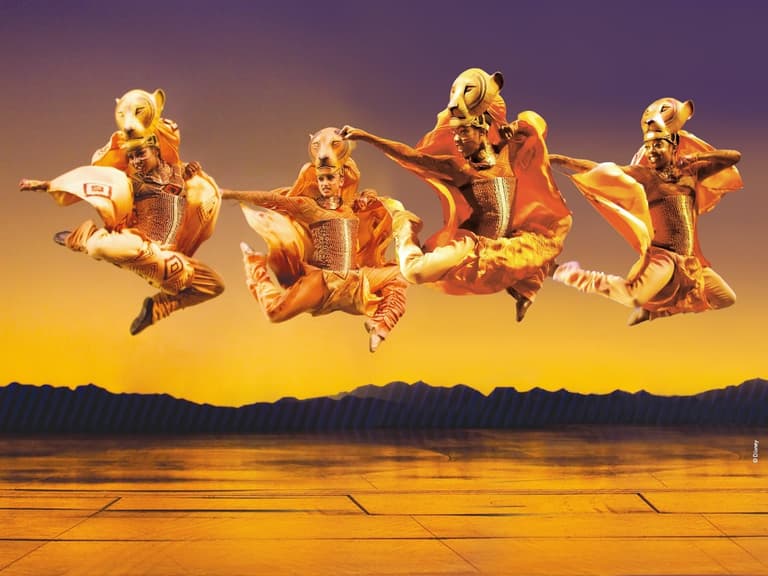 The ensemble of The Lion King leaping across the stage against a sunrise backdrop at the Lyceum Theatre