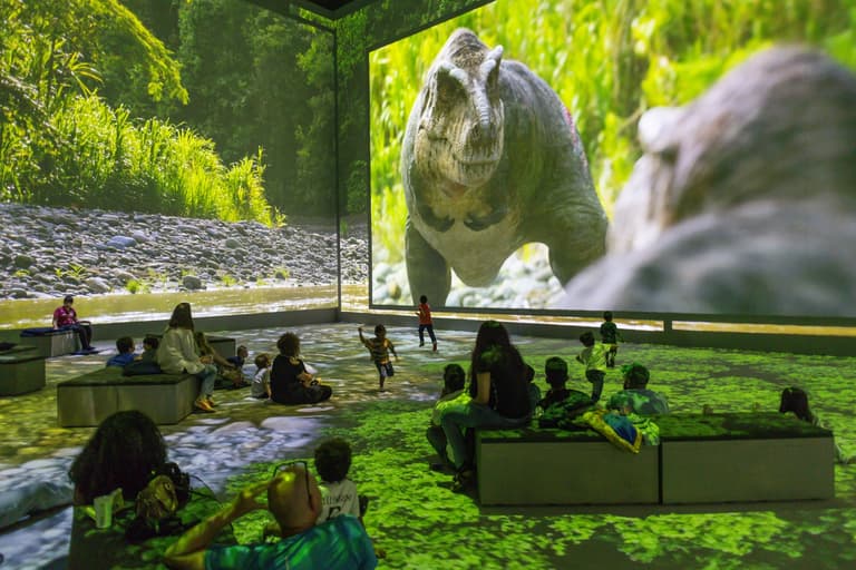 Families watching a life-size projected dinosaur at the Prehistoric Planet experience at Lightroom, King's Cross