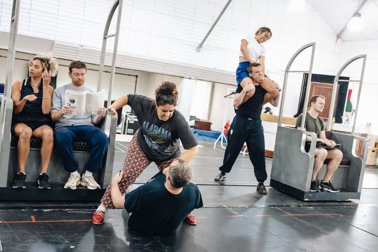 Cast members clamber over a mock train carriage in rehearsal for The Comedy About Spies