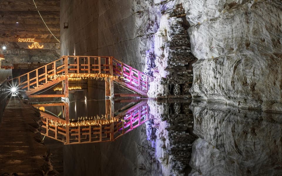 Wooden bridge over a reflective underground lake in Salina Turda salt mine near Bucharest