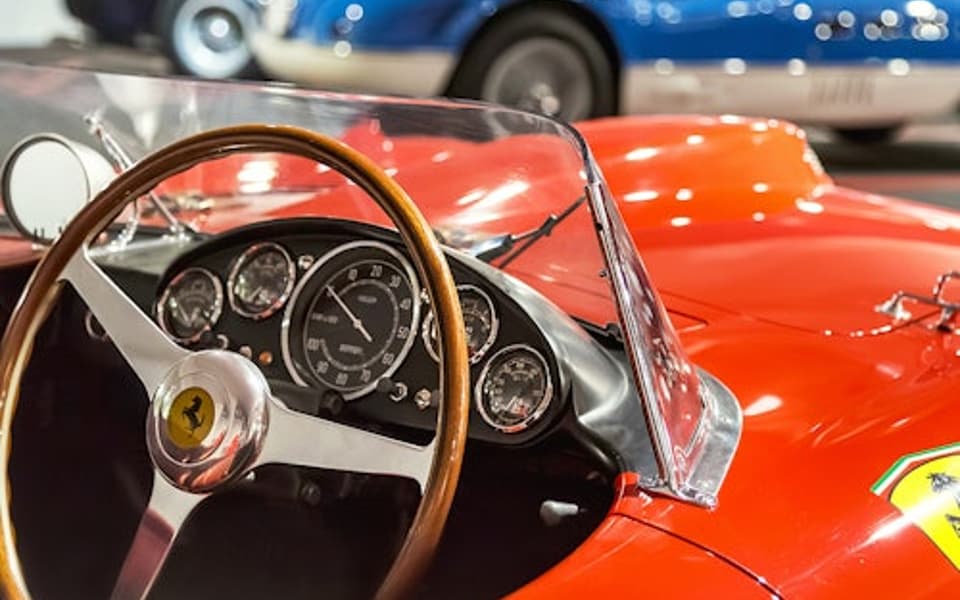 Classic red Ferrari racing car with wooden steering wheel beside a blue Ferrari at the Maranello museum