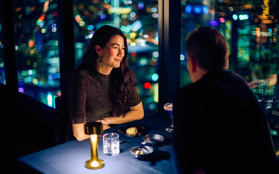 Couple dining at a high-rise restaurant in Melbourne with city skyline lights through tall windows