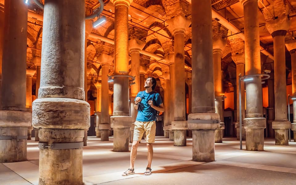 Tourist looking up among warm-lit stone columns inside the Basilica Cistern in Istanbul