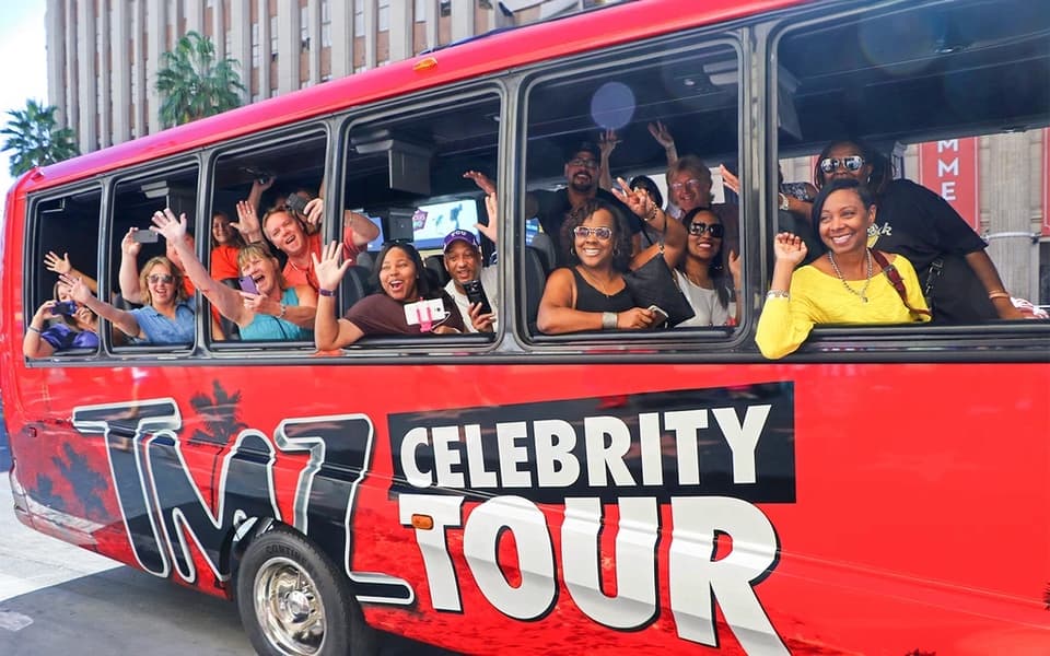 Red TMZ Celebrity Tour open-air bus full of waving passengers in Los Angeles